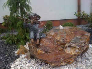 Harasimowicz ogrody - Figura z brązu - chłopiec w kapeluszu z fletem siedzący na kamieniu